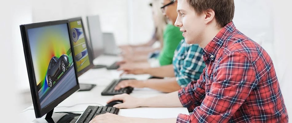 A row of college students sitting in a computer lab, working on desktop monitors with simulation software on the screens.